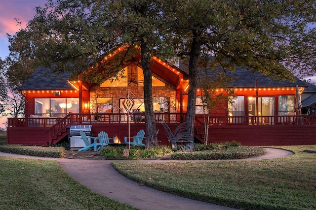 back house at dusk featuring a deck and a lawn