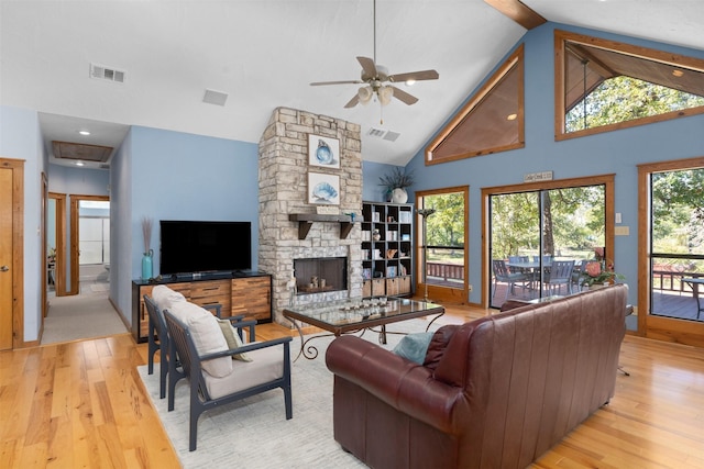 living room with light wood-type flooring, ceiling fan, a stone fireplace, and high vaulted ceiling