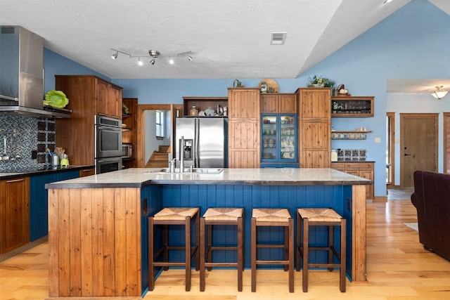 kitchen featuring appliances with stainless steel finishes, a kitchen island with sink, tasteful backsplash, and wall chimney range hood