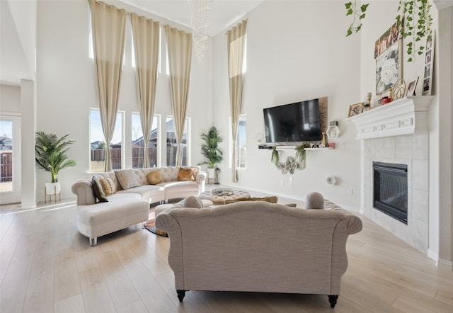 living room with a tiled fireplace, light hardwood / wood-style flooring, and a high ceiling