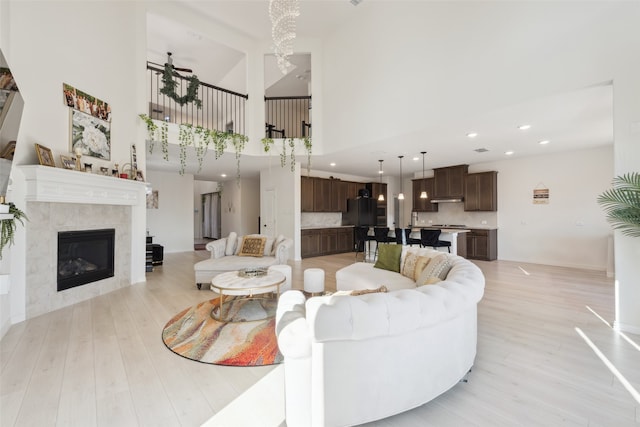 living room featuring a high ceiling, light wood-type flooring, a chandelier, and a fireplace