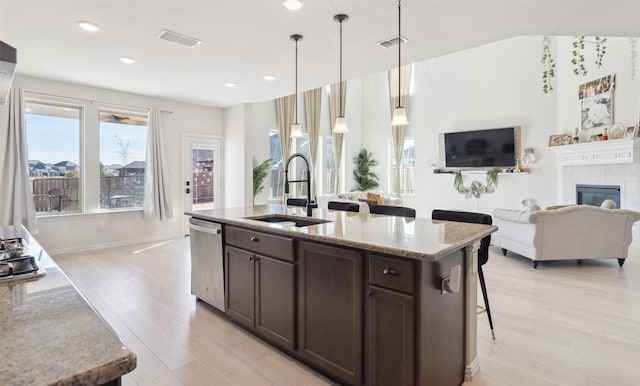 kitchen featuring a tiled fireplace, stainless steel dishwasher, light stone countertops, and sink