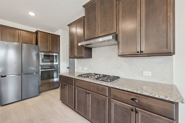 kitchen with light hardwood / wood-style flooring, appliances with stainless steel finishes, dark brown cabinets, light stone counters, and tasteful backsplash