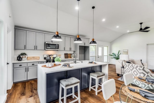 kitchen featuring lofted ceiling, gray cabinets, hanging light fixtures, appliances with stainless steel finishes, and an island with sink