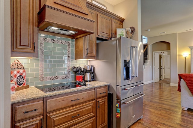 kitchen with black electric stovetop, decorative backsplash, premium range hood, light wood-type flooring, and high end refrigerator