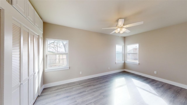 unfurnished bedroom featuring ceiling fan, a closet, light hardwood / wood-style flooring, and multiple windows