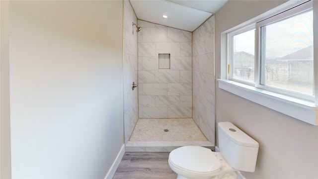 bathroom featuring toilet, wood-type flooring, plenty of natural light, and tiled shower