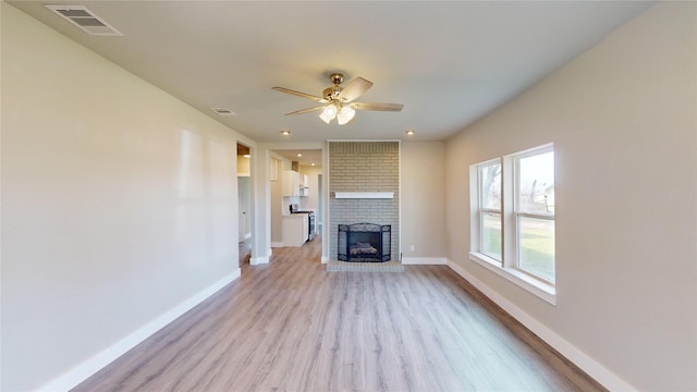 unfurnished living room featuring ceiling fan, light wood-type flooring, and a brick fireplace