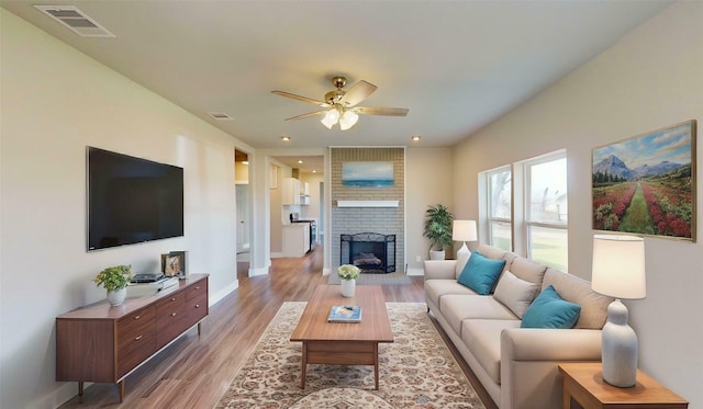 living room with a brick fireplace, light hardwood / wood-style flooring, and ceiling fan