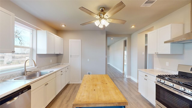 kitchen featuring white cabinets, appliances with stainless steel finishes, wall chimney exhaust hood, butcher block counters, and sink