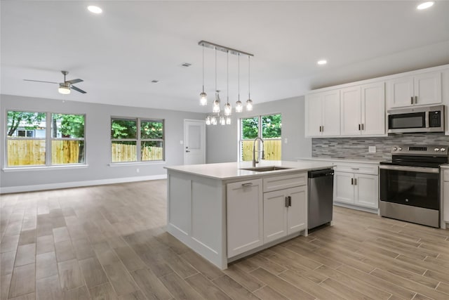 kitchen featuring white cabinets, appliances with stainless steel finishes, decorative light fixtures, sink, and a center island with sink