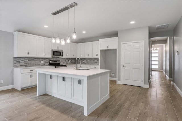 kitchen featuring pendant lighting, sink, appliances with stainless steel finishes, an island with sink, and white cabinets