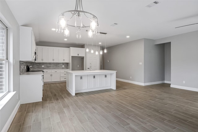 kitchen featuring hanging light fixtures, white cabinets, sink, and an island with sink