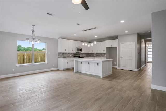 kitchen featuring hanging light fixtures, white cabinets, a kitchen island with sink, and appliances with stainless steel finishes