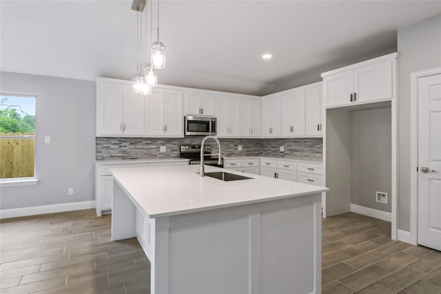 kitchen featuring sink, hanging light fixtures, an island with sink, stainless steel appliances, and white cabinets