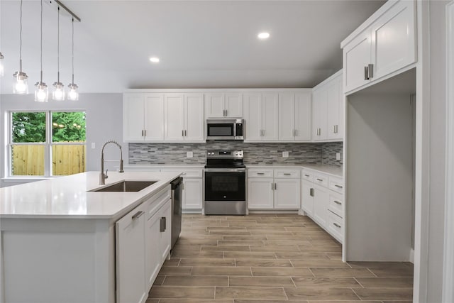 kitchen featuring white cabinets, appliances with stainless steel finishes, an island with sink, sink, and hanging light fixtures