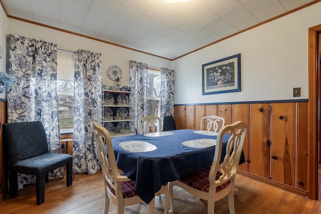 dining room featuring wood walls, light hardwood / wood-style flooring, and ornamental molding