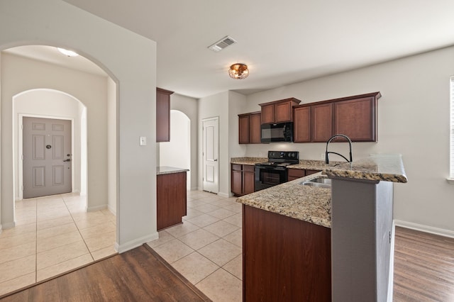 kitchen featuring kitchen peninsula, light tile patterned flooring, light stone countertops, black appliances, and sink