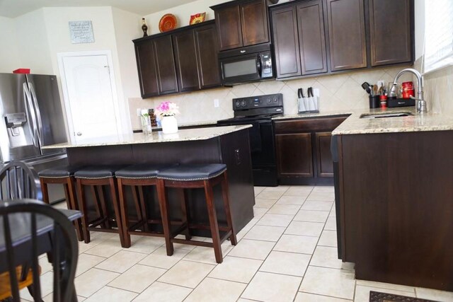 kitchen with light tile patterned floors, tasteful backsplash, a kitchen breakfast bar, black appliances, and a sink