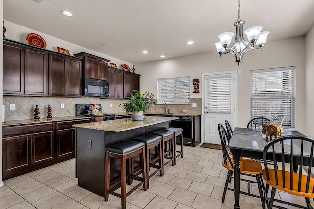 kitchen featuring stove, black microwave, backsplash, a chandelier, and a kitchen bar