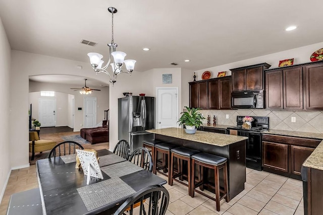 kitchen featuring black appliances, arched walkways, a kitchen island, dark brown cabinetry, and tasteful backsplash