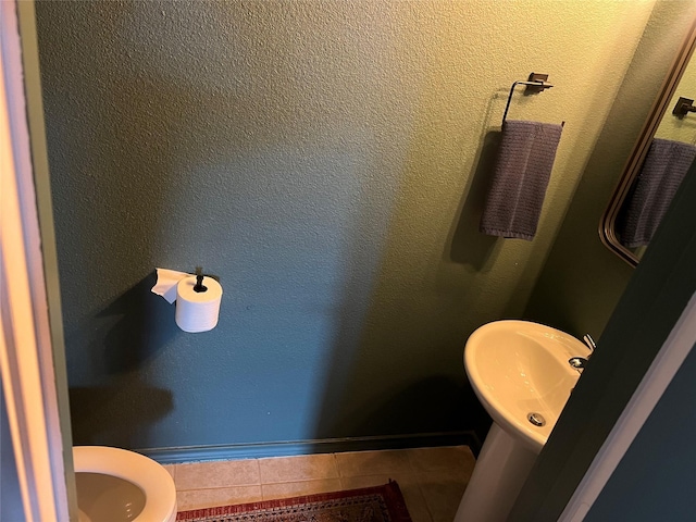 bathroom with a sink, a textured wall, tile patterned flooring, and toilet