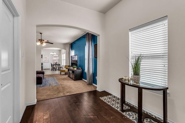 hall featuring arched walkways, wood-type flooring, baseboards, and a chandelier