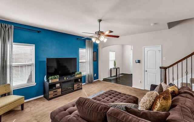 living area with arched walkways, carpet, ceiling fan, and stairway