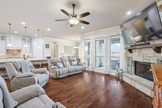 living room featuring ceiling fan with notable chandelier and a stone fireplace