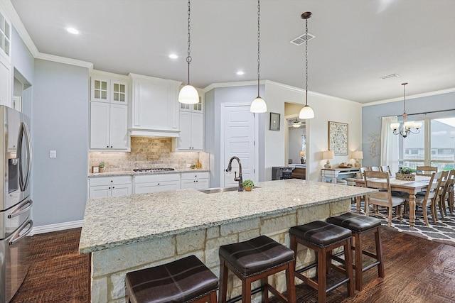 kitchen with white cabinetry, appliances with stainless steel finishes, a kitchen island with sink, and a notable chandelier