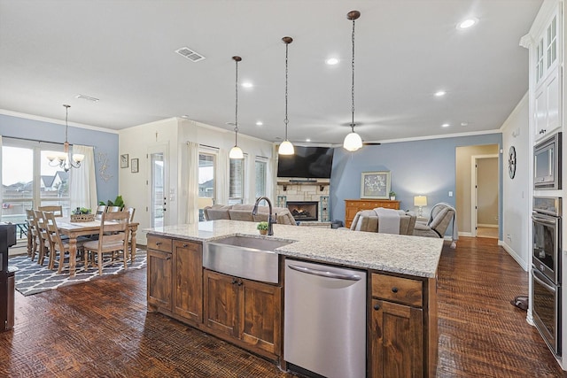 kitchen featuring white cabinets, appliances with stainless steel finishes, a stone fireplace, sink, and a notable chandelier