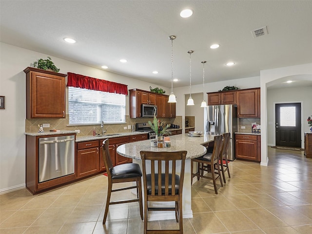 kitchen featuring a center island, sink, hanging light fixtures, stainless steel appliances, and light tile patterned floors