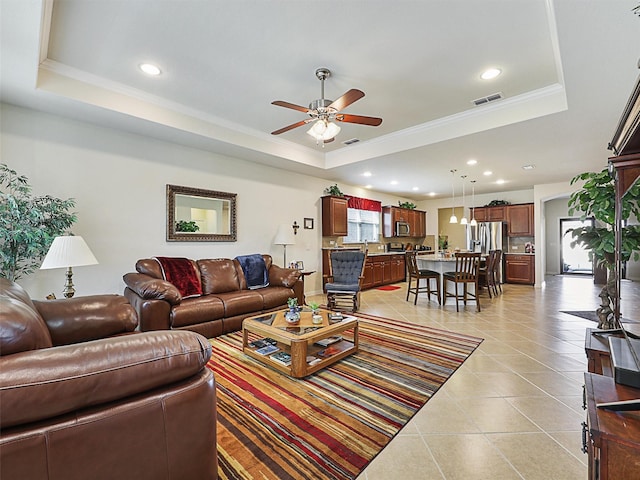 tiled living room with ceiling fan, a wealth of natural light, and a raised ceiling