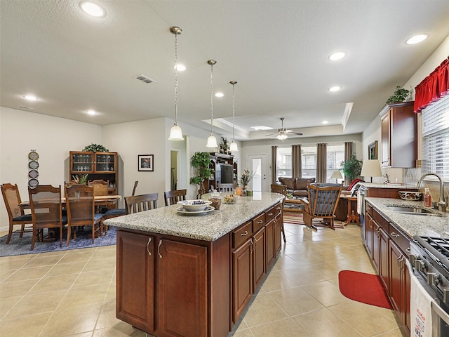 kitchen featuring ceiling fan, a tray ceiling, a kitchen island, pendant lighting, and sink