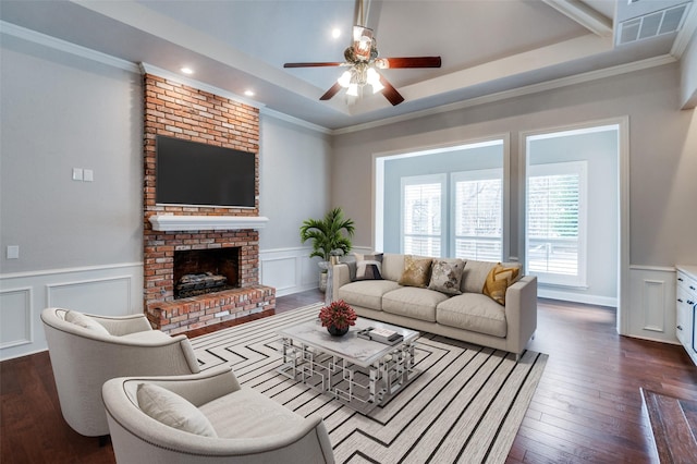 living room with ornamental molding, dark hardwood / wood-style flooring, a brick fireplace, and a raised ceiling