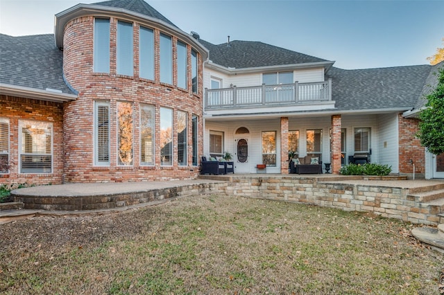 rear view of house featuring a balcony, a patio area, and a lawn