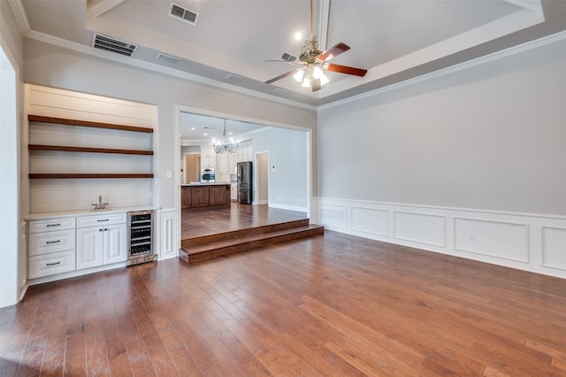 unfurnished living room featuring crown molding, dark hardwood / wood-style flooring, a raised ceiling, and wine cooler