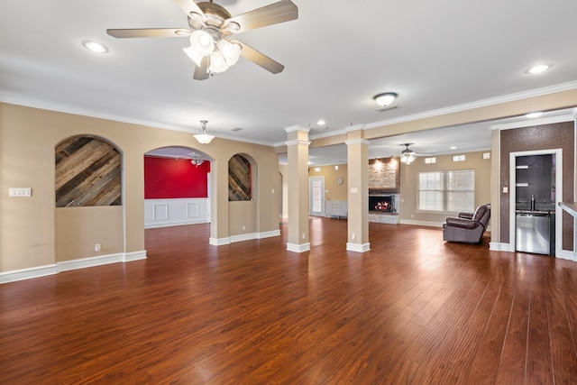 unfurnished living room with ornate columns, crown molding, a large fireplace, and ceiling fan