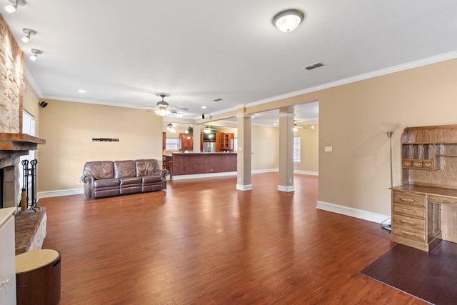 living room featuring dark hardwood / wood-style floors, ornamental molding, a stone fireplace, and decorative columns