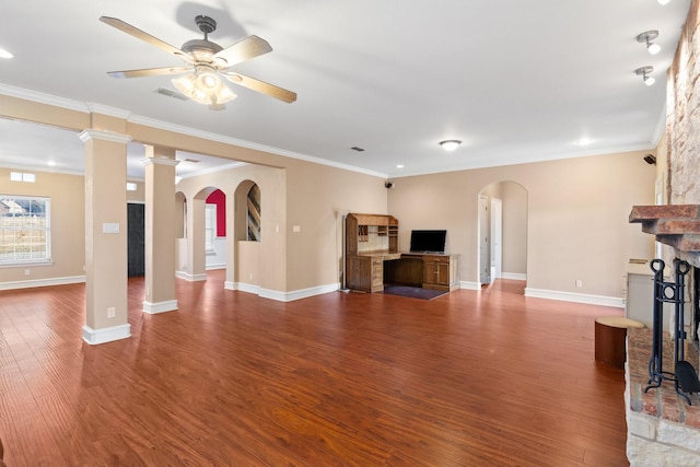 unfurnished living room featuring hardwood / wood-style flooring, ceiling fan, ornamental molding, a large fireplace, and ornate columns