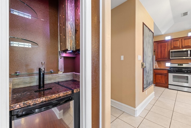 kitchen featuring light tile patterned floors, vaulted ceiling, stainless steel appliances, and dark stone counters