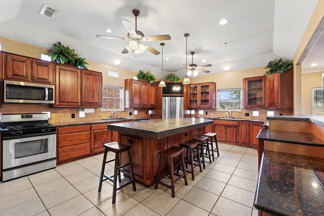 kitchen featuring light tile patterned flooring, a kitchen bar, a center island, appliances with stainless steel finishes, and backsplash