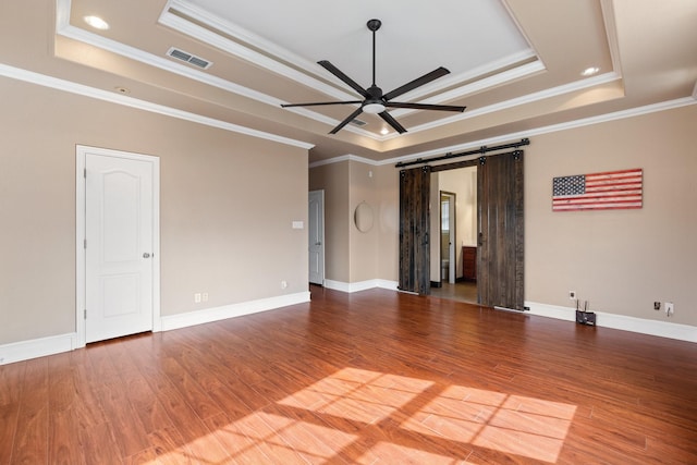 unfurnished room featuring ornamental molding, a barn door, a raised ceiling, and hardwood / wood-style floors