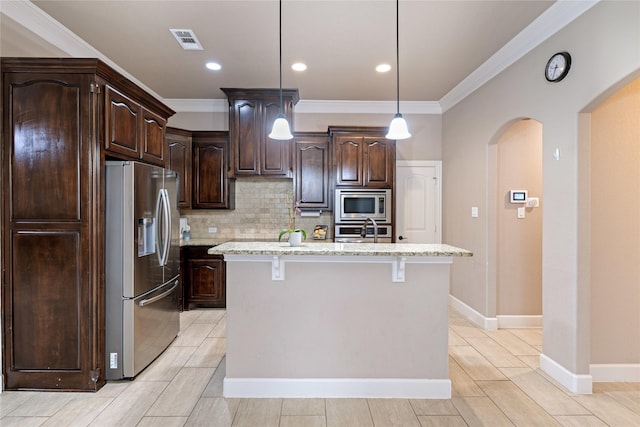 kitchen with pendant lighting, dark brown cabinets, stainless steel appliances, light stone countertops, and an island with sink