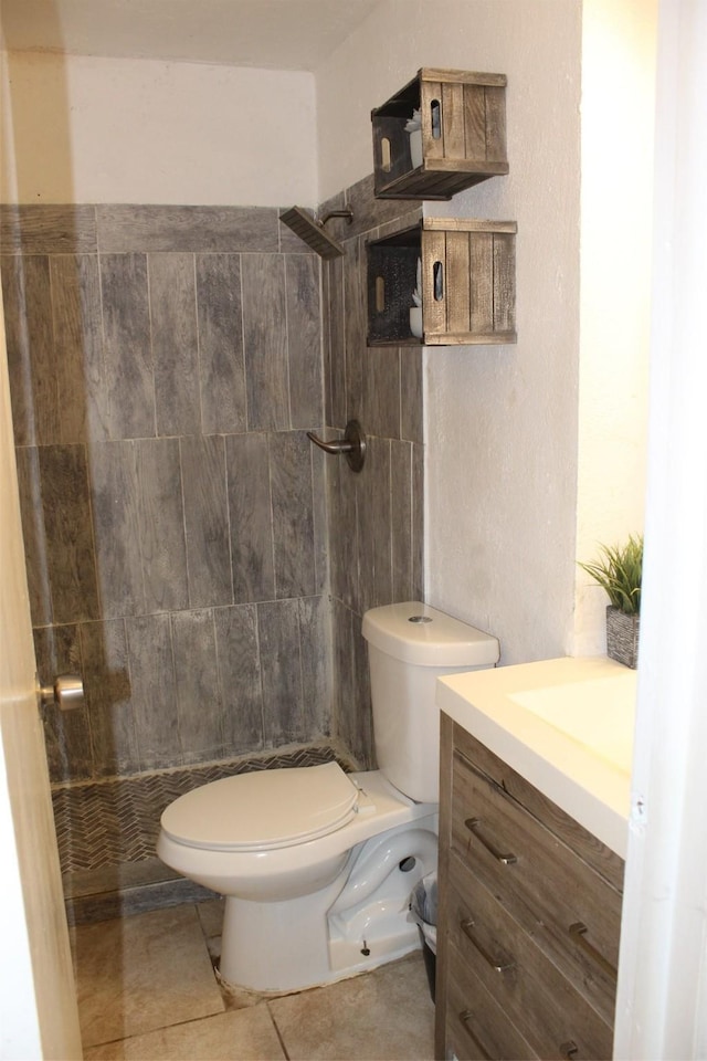 bathroom featuring a tile shower, tile patterned flooring, vanity, and toilet