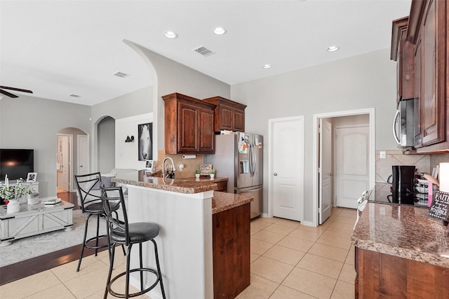 kitchen featuring stone counters, appliances with stainless steel finishes, a kitchen breakfast bar, light tile patterned flooring, and decorative backsplash