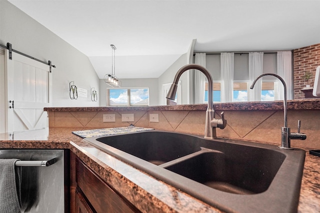 kitchen with sink, vaulted ceiling, hanging light fixtures, stainless steel dishwasher, and a barn door