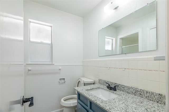 bathroom featuring toilet, vanity, and tile walls