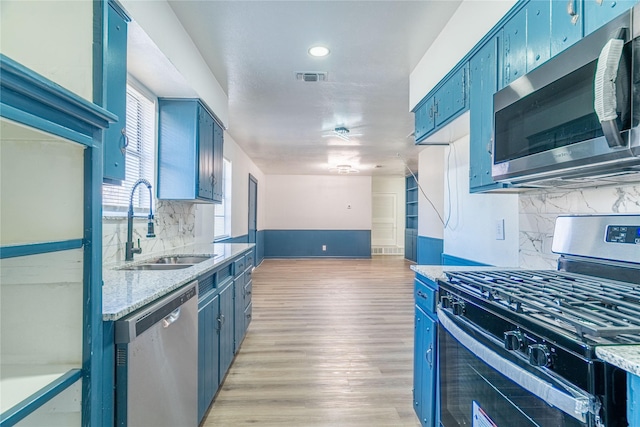 kitchen featuring backsplash, sink, stainless steel appliances, blue cabinets, and light stone counters