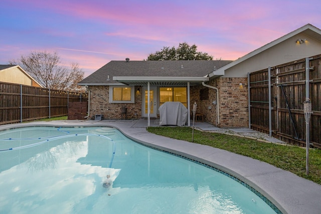 pool at dusk featuring a grill and a patio